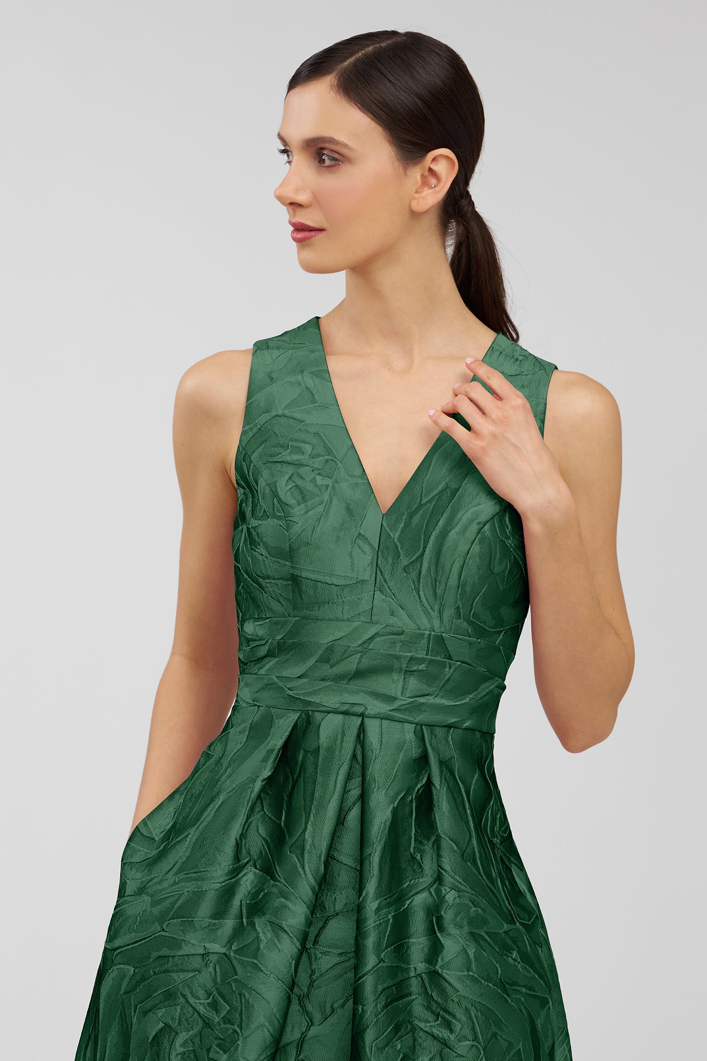 Woman wearing a green dress with a subtle pattern on a light gray background