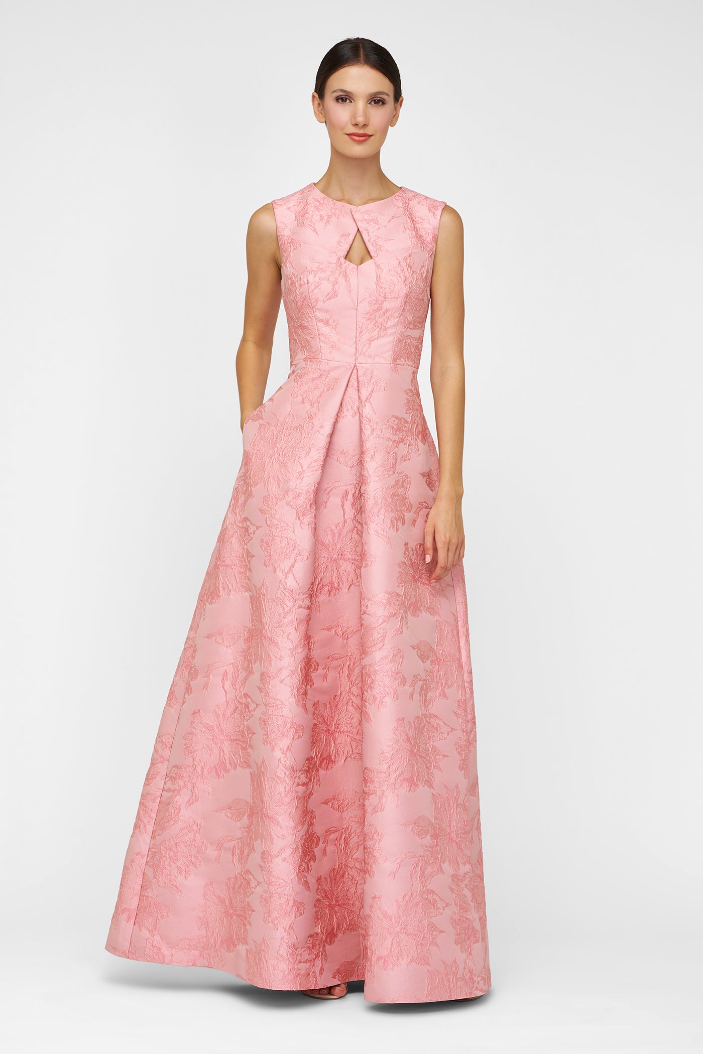 A woman wearing a blush floral jacquard gown with a sculpted keyhole neckline and structured A-line skirt.