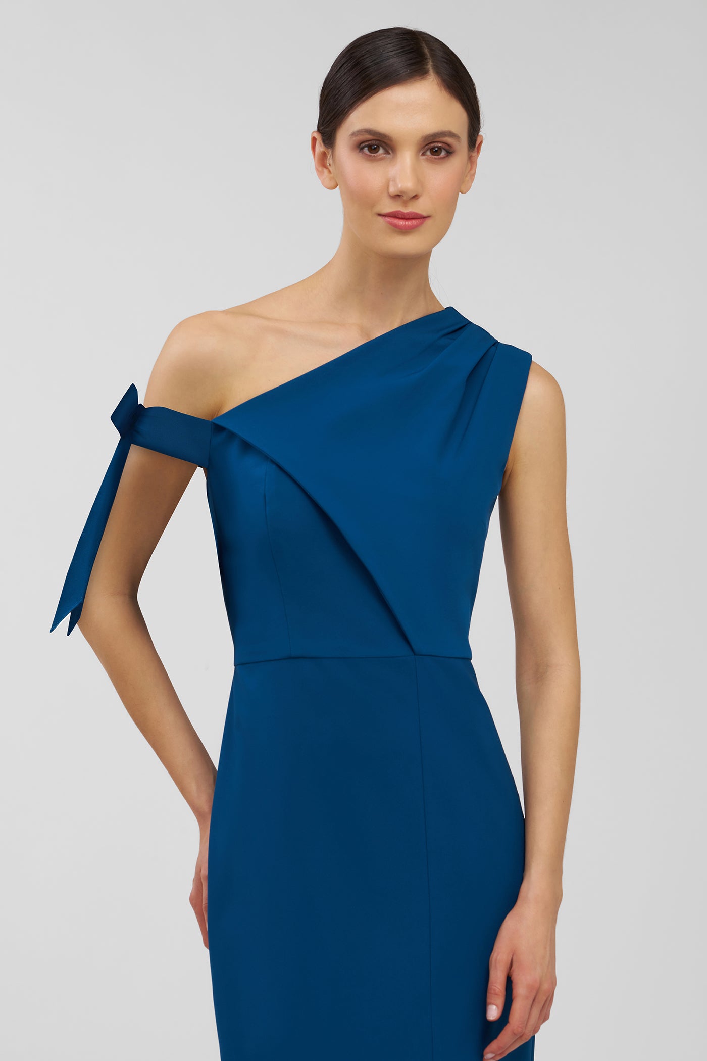 Woman wearing a blue one-shoulder dress with a bow detail on a gray background