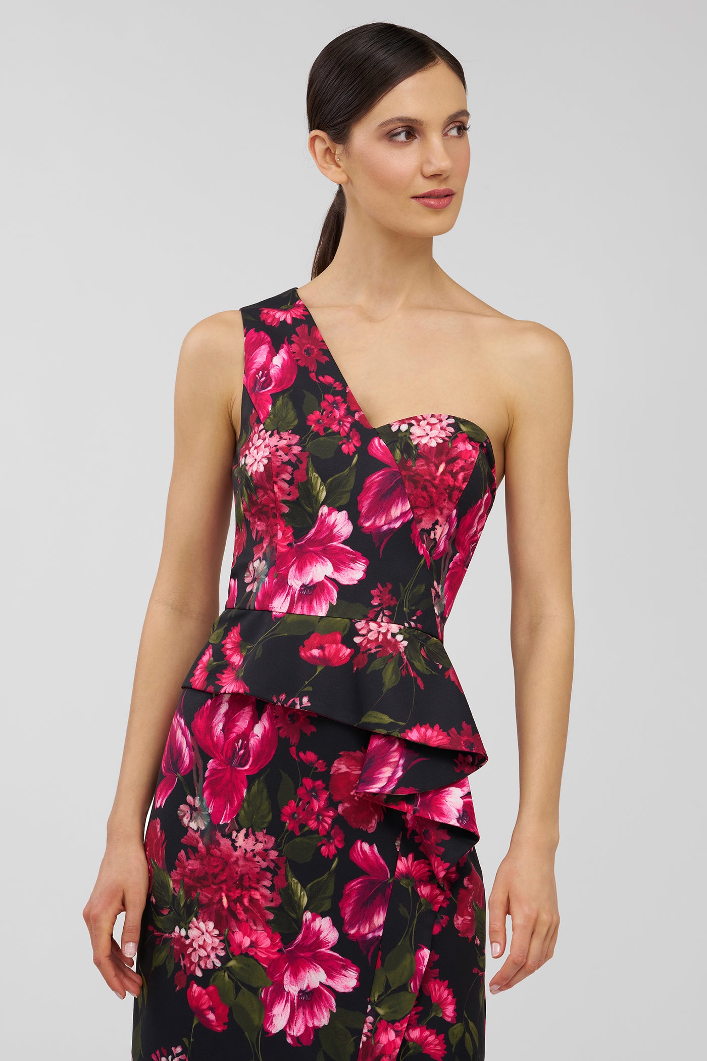 Woman wearing a black floral one-shoulder dress on a light gray background