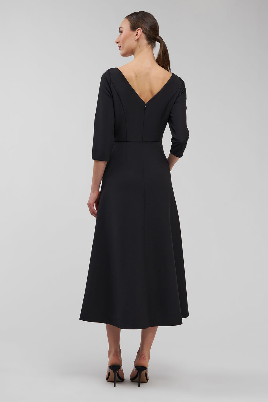 Woman wearing a black dress with a V-neckline and three-quarter sleeves on a gray background