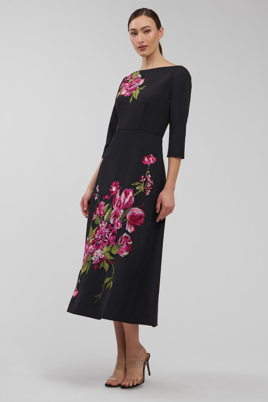 Woman wearing a black dress with floral embroidery on a gray background