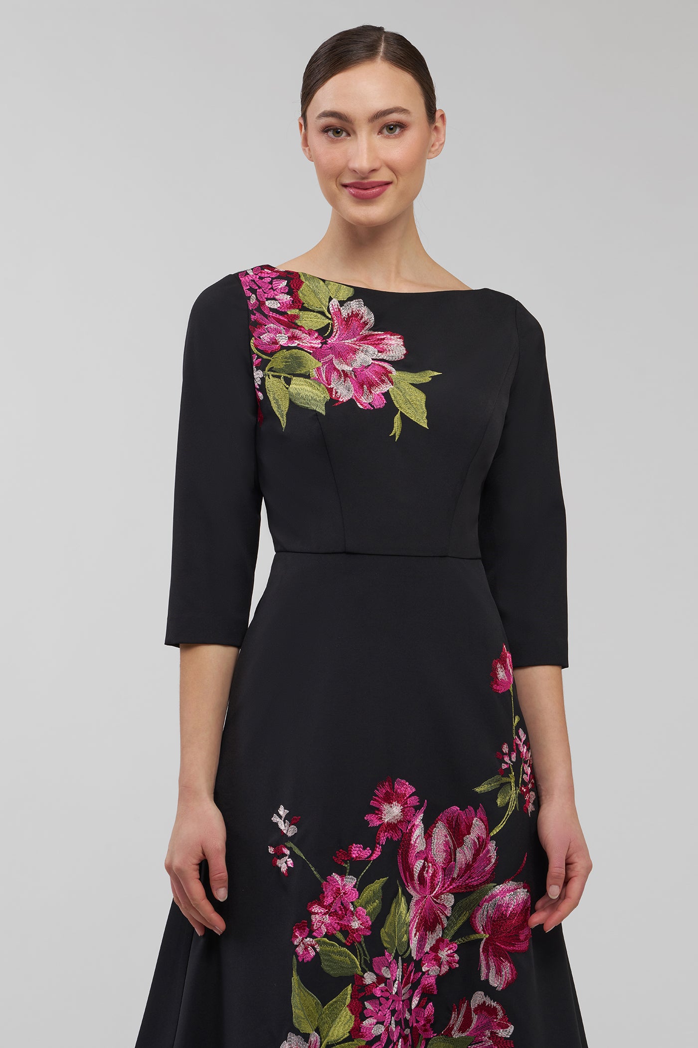 Woman wearing a black dress with floral embroidery on a gray background