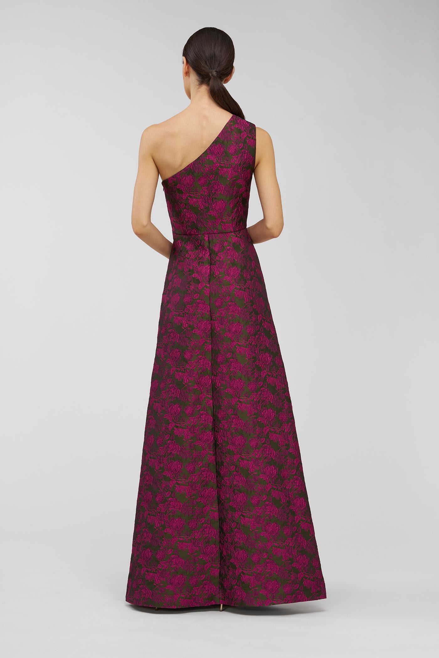 Woman wearing a one-shoulder patterned dress on a light gray background