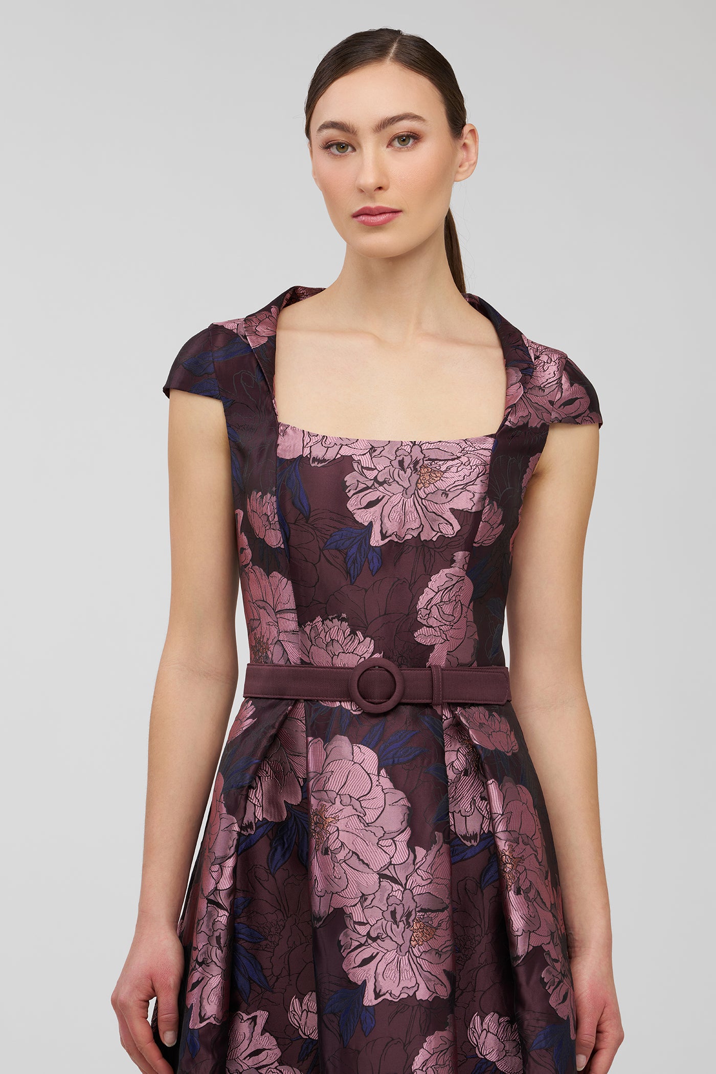 Woman wearing a floral dress with a belt on a plain background