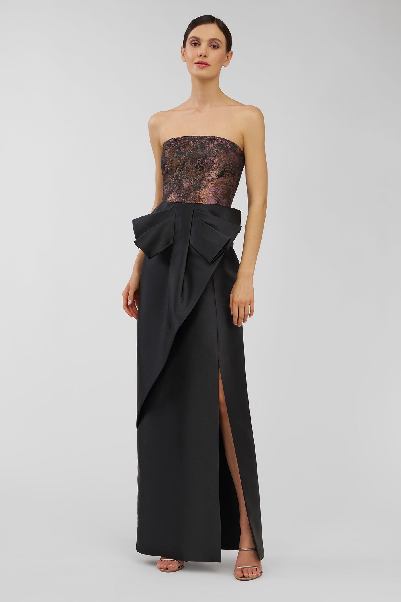 Woman wearing a black strapless gown with a large bow on a light gray background