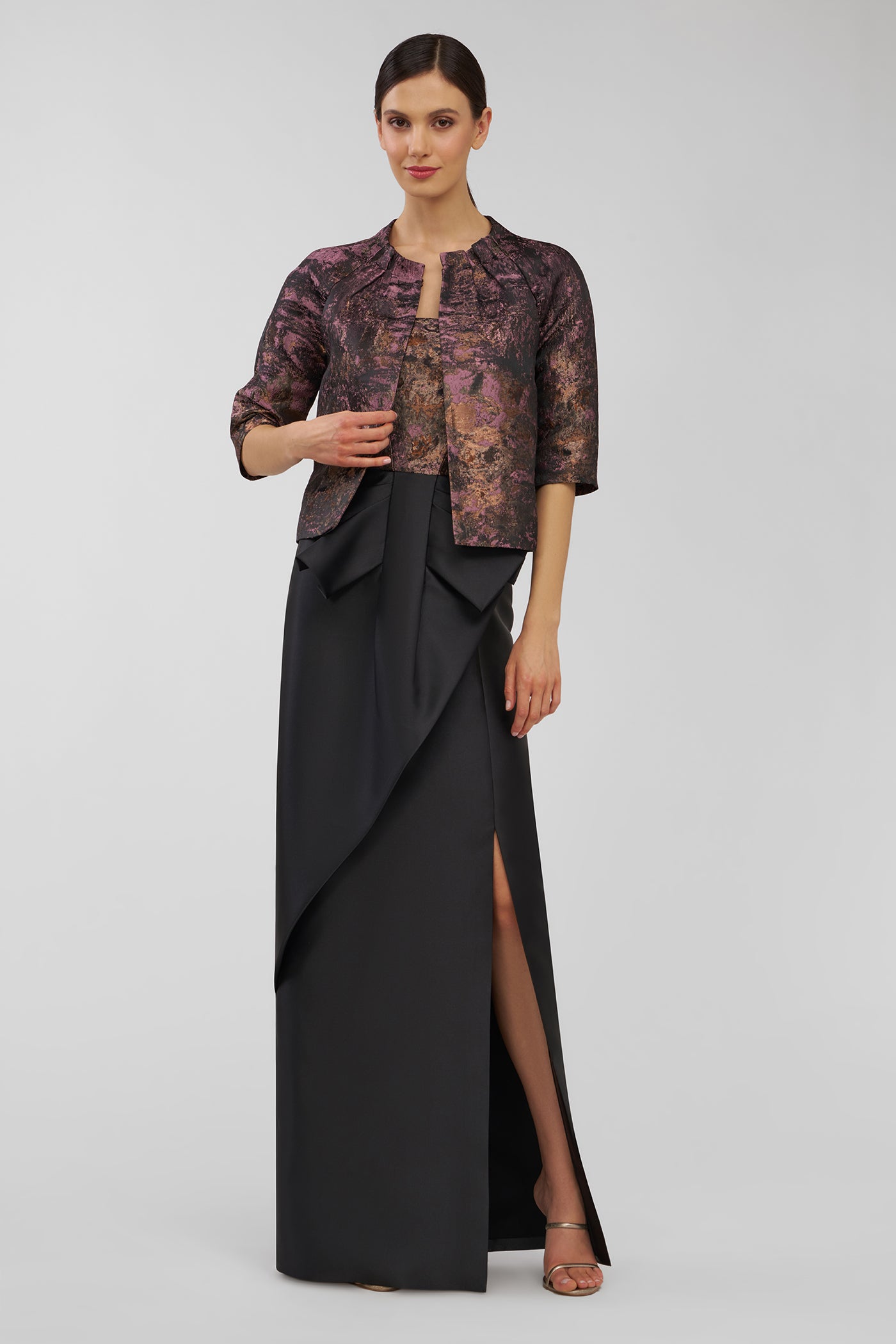 Woman wearing a black and patterned top with a long black skirt on a gray background