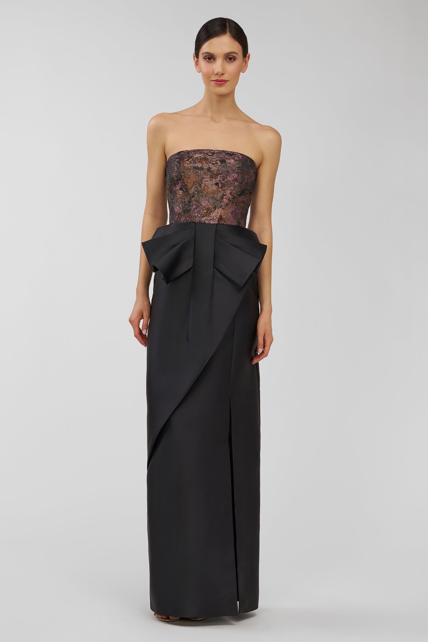 Woman wearing a strapless black evening gown with a large bow on a white background