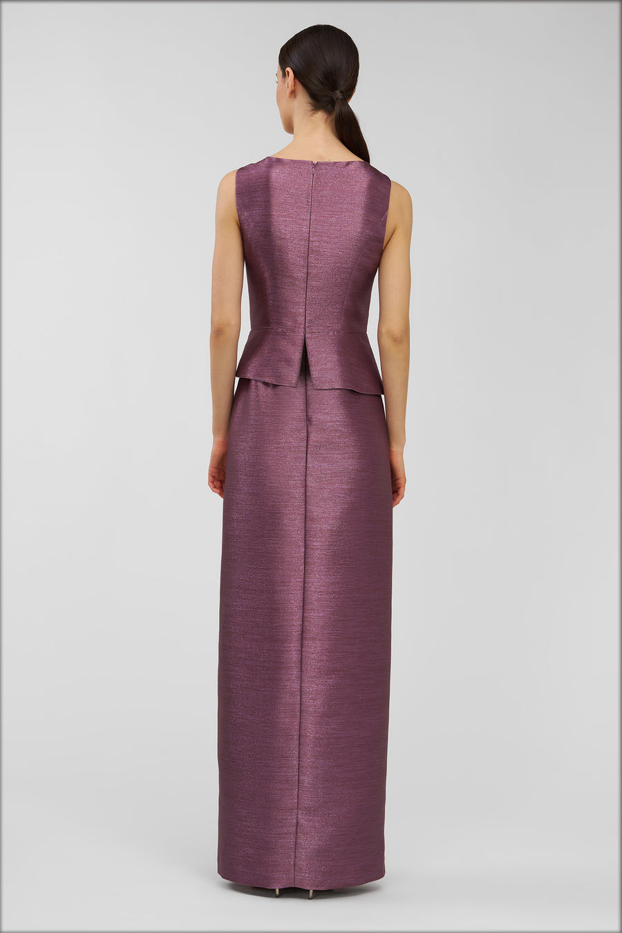 Woman wearing a long purple dress with a peplum detail on a gray background