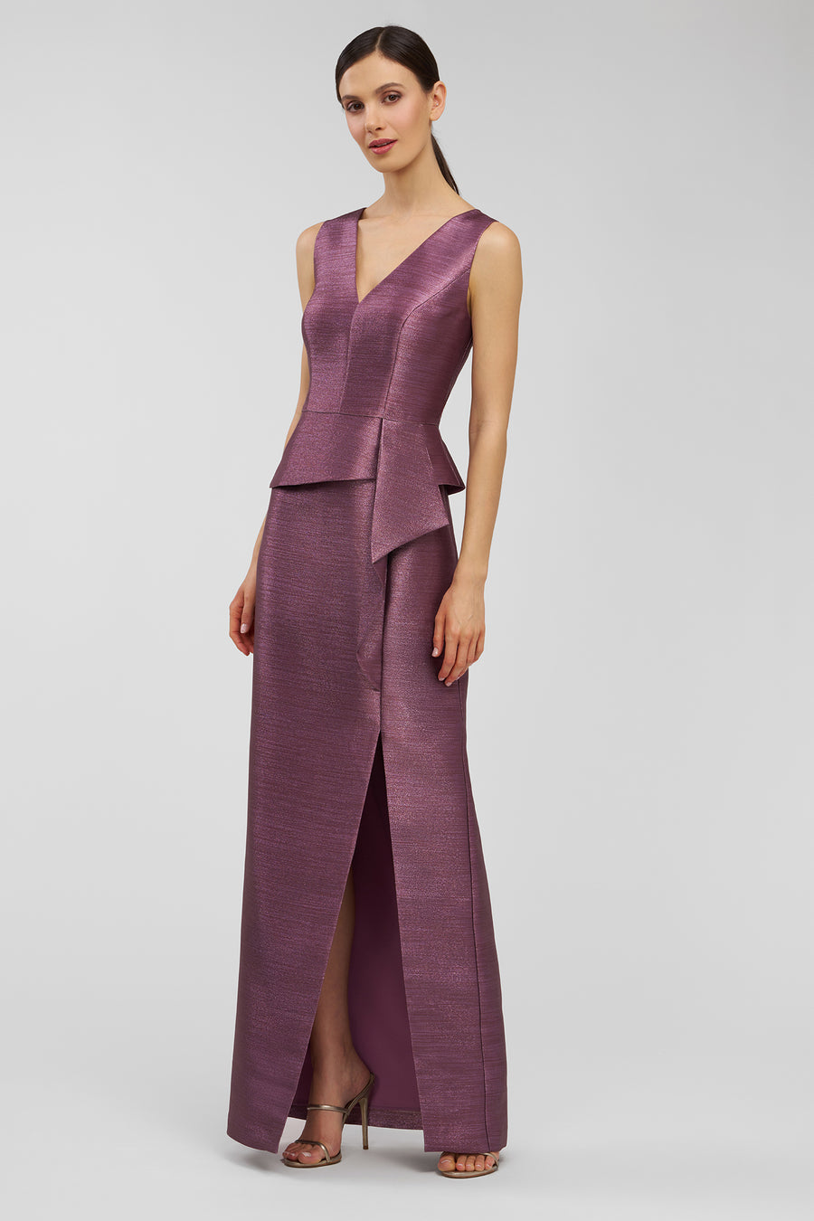 Woman wearing a purple evening gown with a V-neck and peplum detail on a light gray background