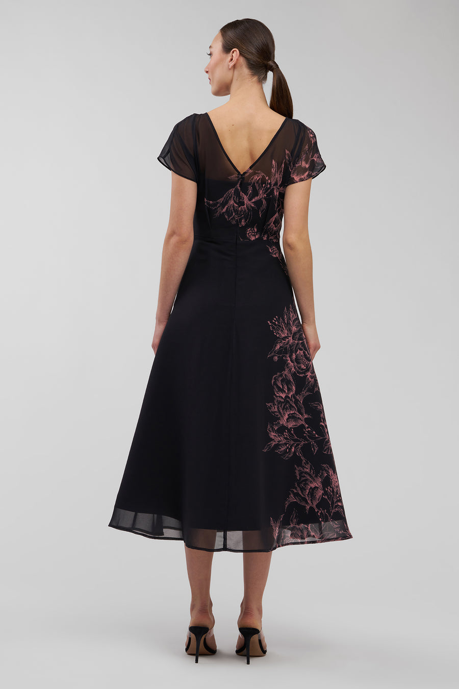 Woman wearing a black dress with floral embroidery on a gray background