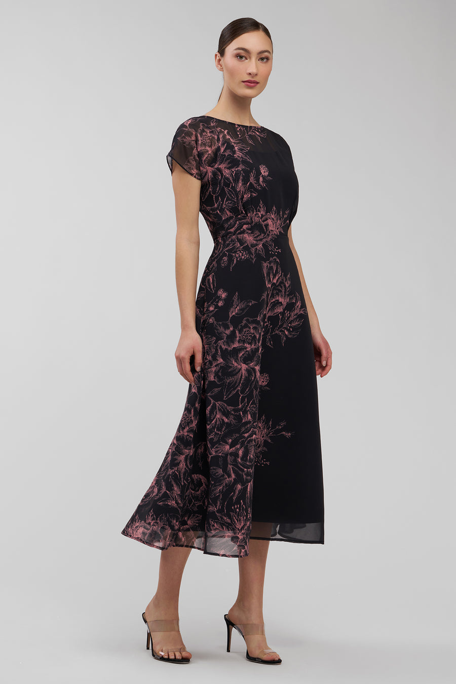 Woman wearing a black dress with pink floral pattern on a gray background