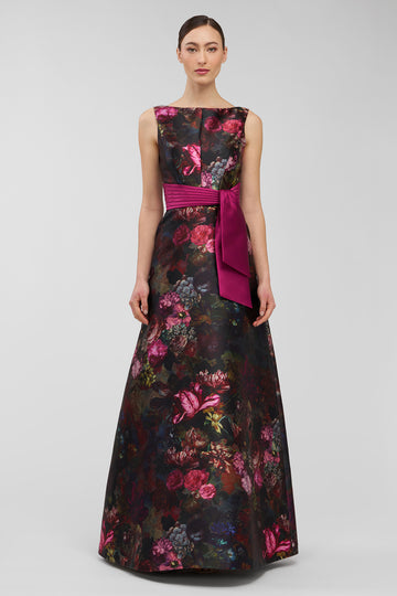 Woman wearing a floral evening gown with a pink belt on a gray background