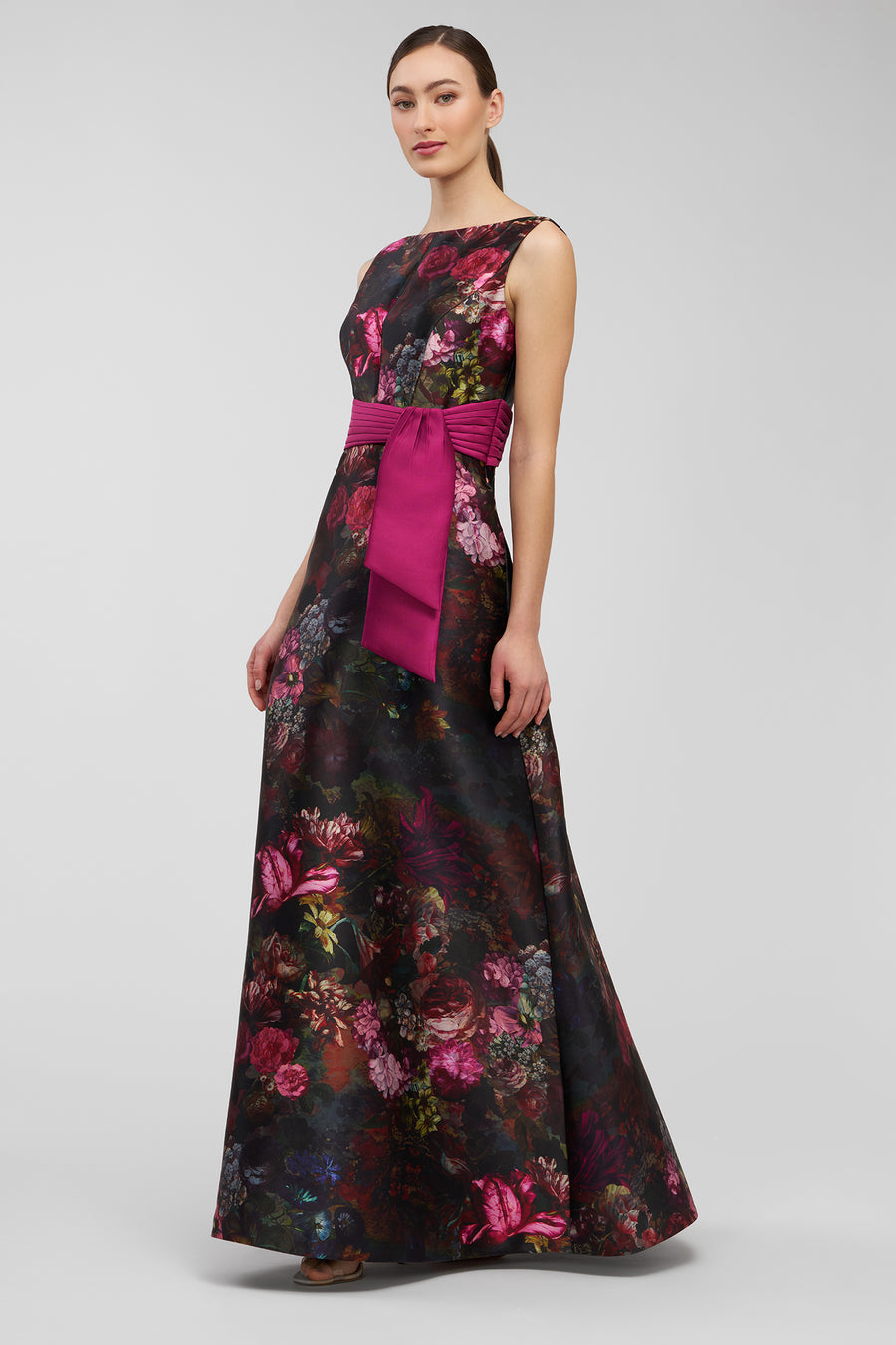 Woman wearing a floral dress with a pink belt on a gray background