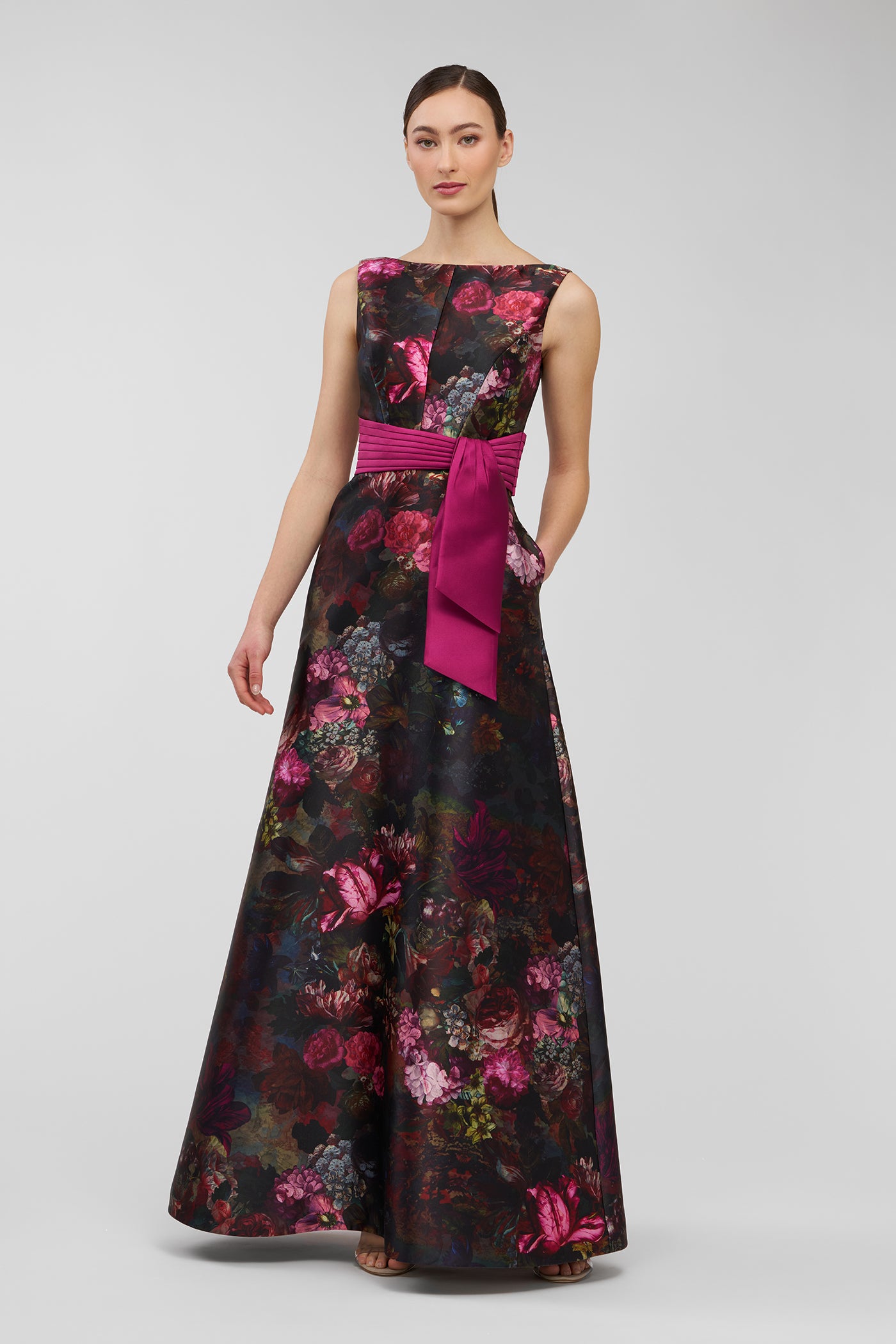 Woman wearing a floral evening gown with a pink belt on a white background
