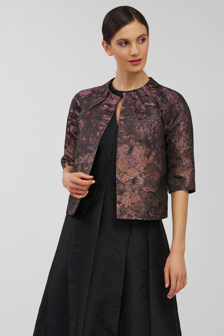 Woman wearing a patterned jacket over a black dress on a gray background