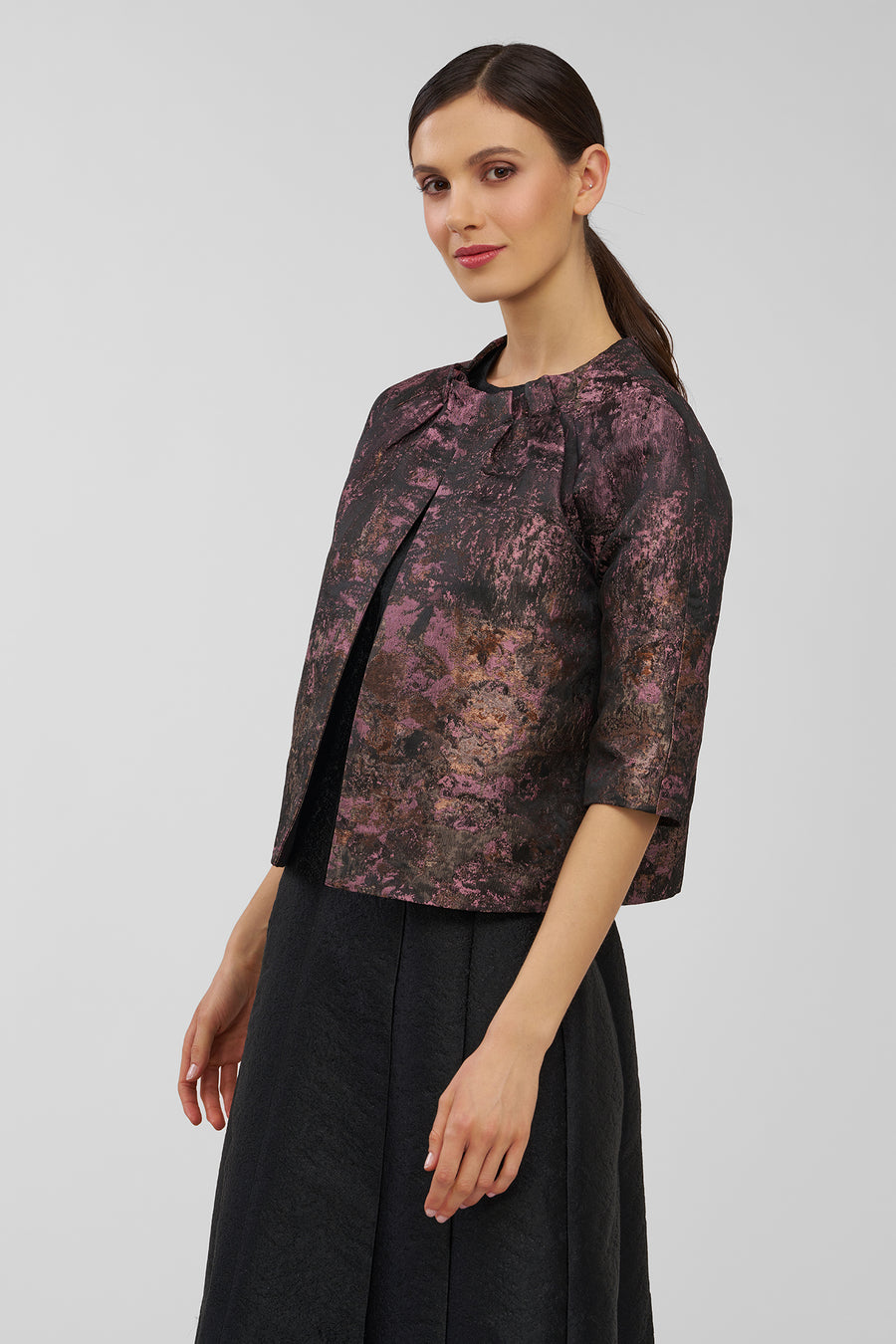 Woman wearing a patterned jacket and black skirt on a plain background