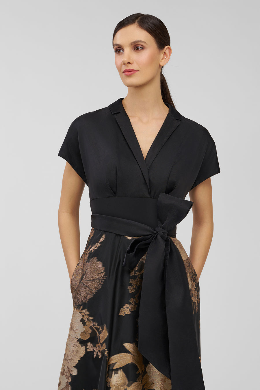Woman wearing a black and gold floral dress on a gray background