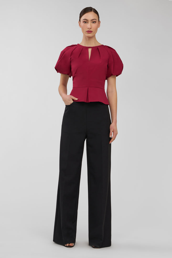Woman wearing a red blouse with puff sleeves and black pants on a white background