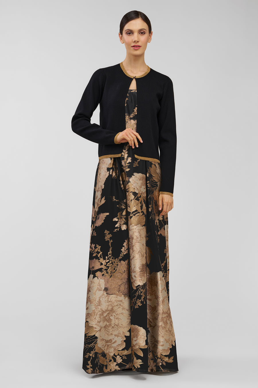 Woman wearing a black top and long, patterned gown on a gray background