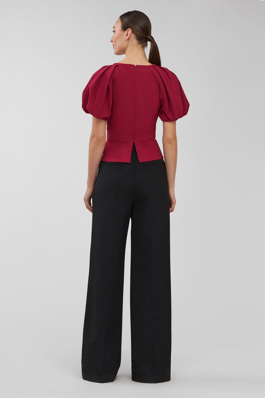Woman wearing a red blouse with puff sleeves and black pants on a gray background