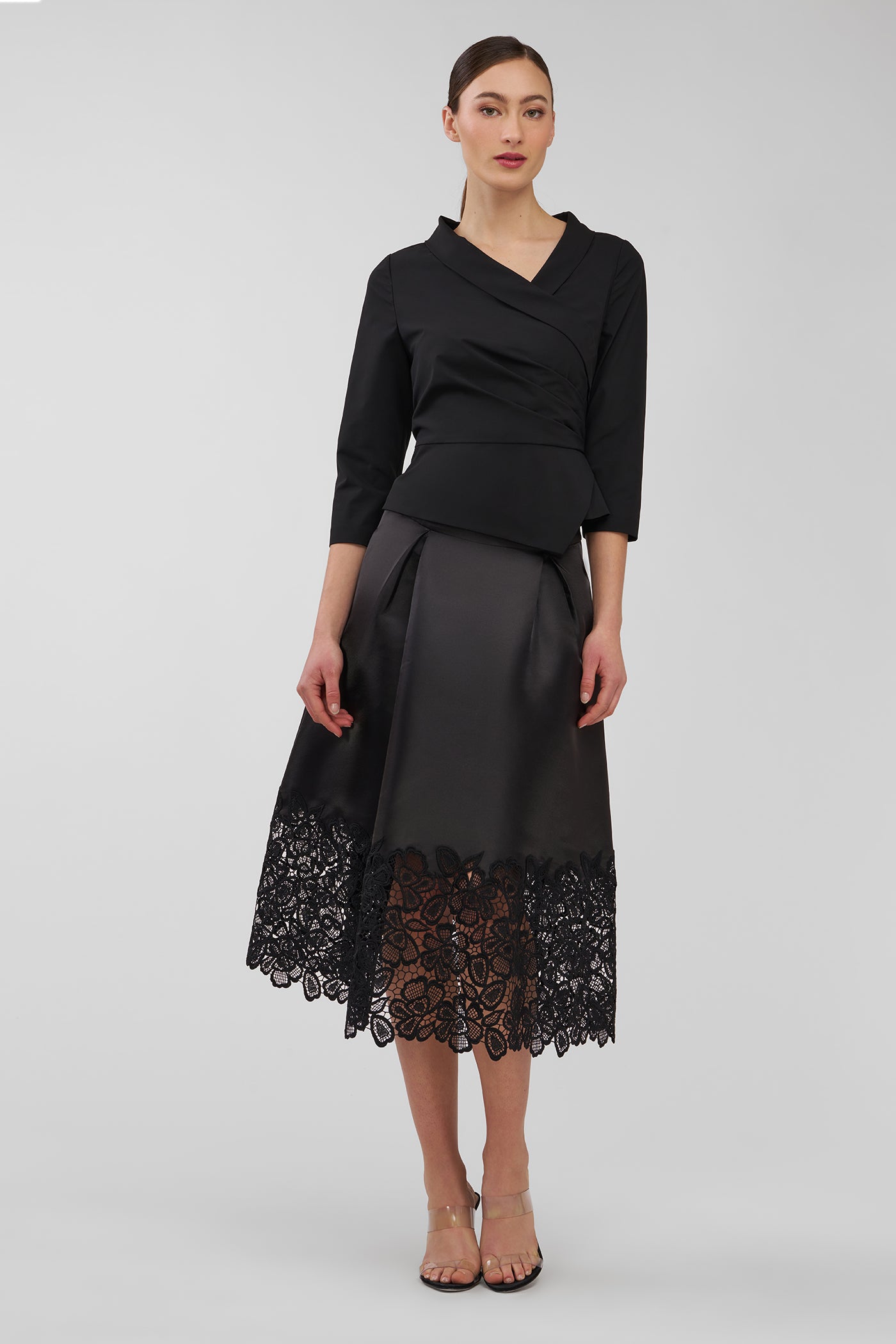 Woman wearing a black top and black skirt with lace hem on a white background