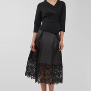 Woman wearing a black top and black skirt with lace hem on a white background