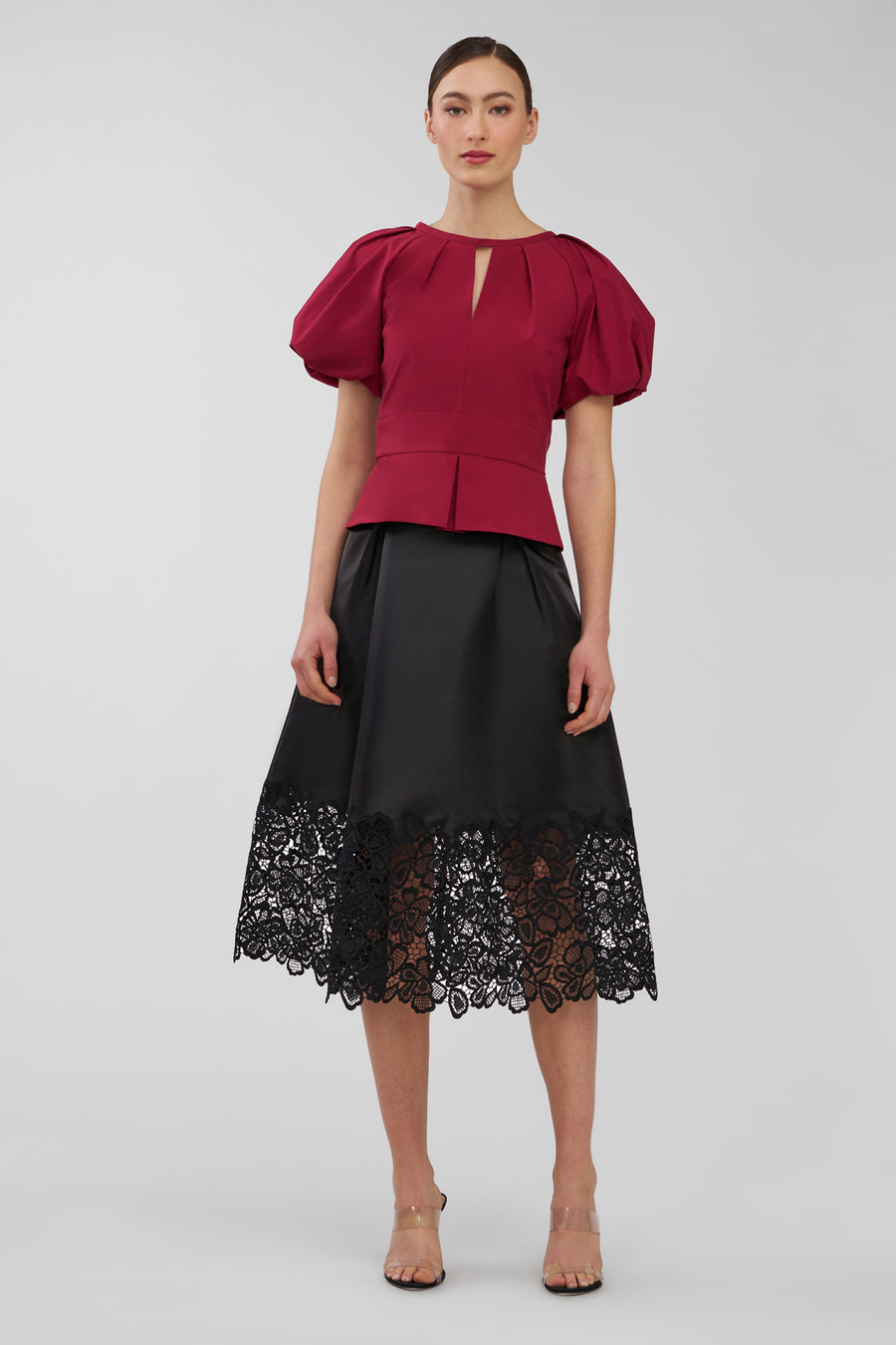 Woman wearing a red top and black skirt with lace details on a white background