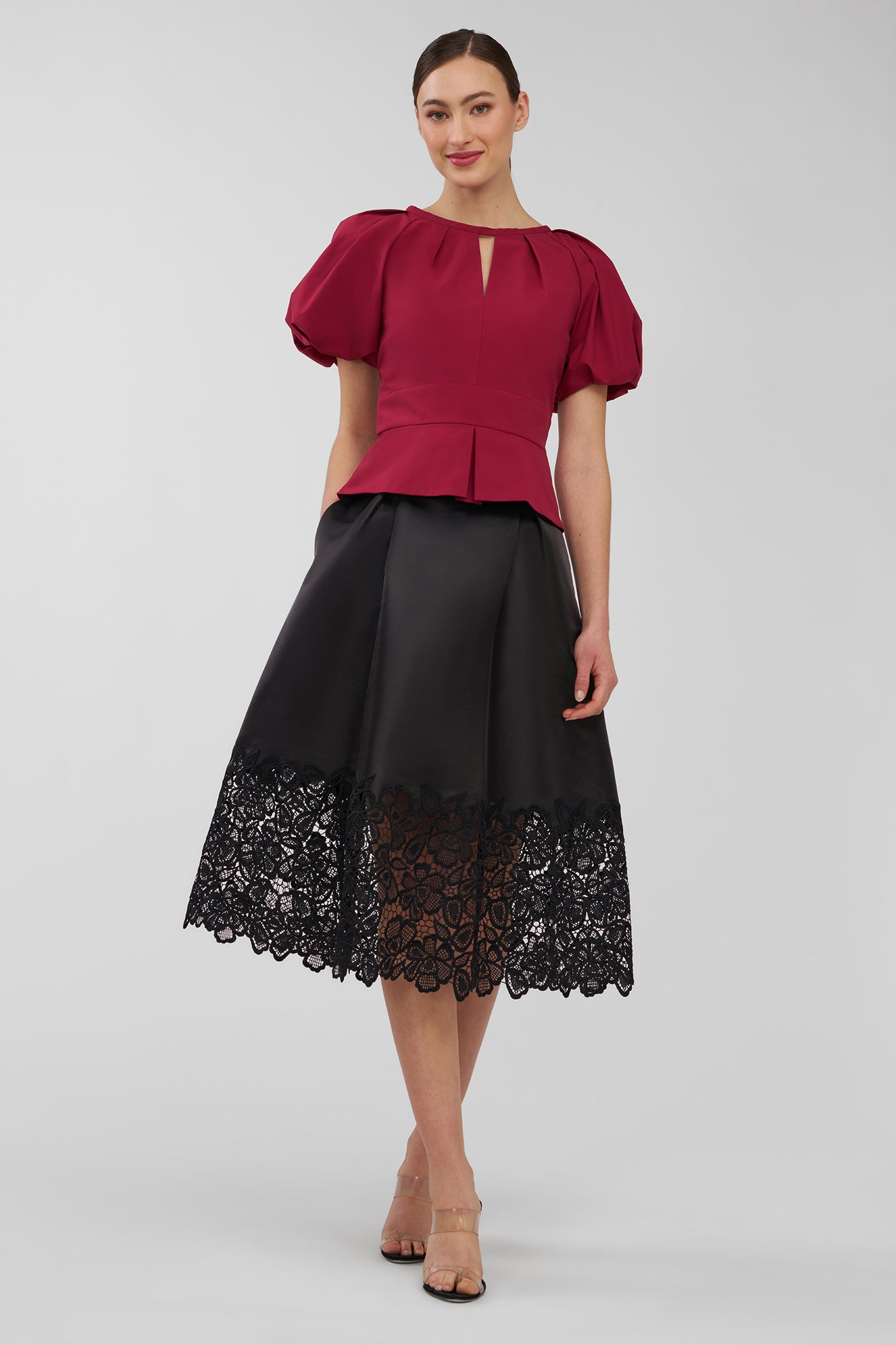 Woman wearing a red top and black skirt with lace details on a white background