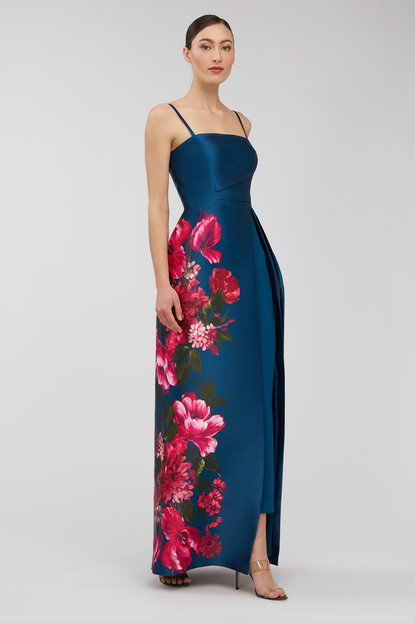 Woman wearing a blue walk thru jumpsuit  with pink floral pattern on a white background