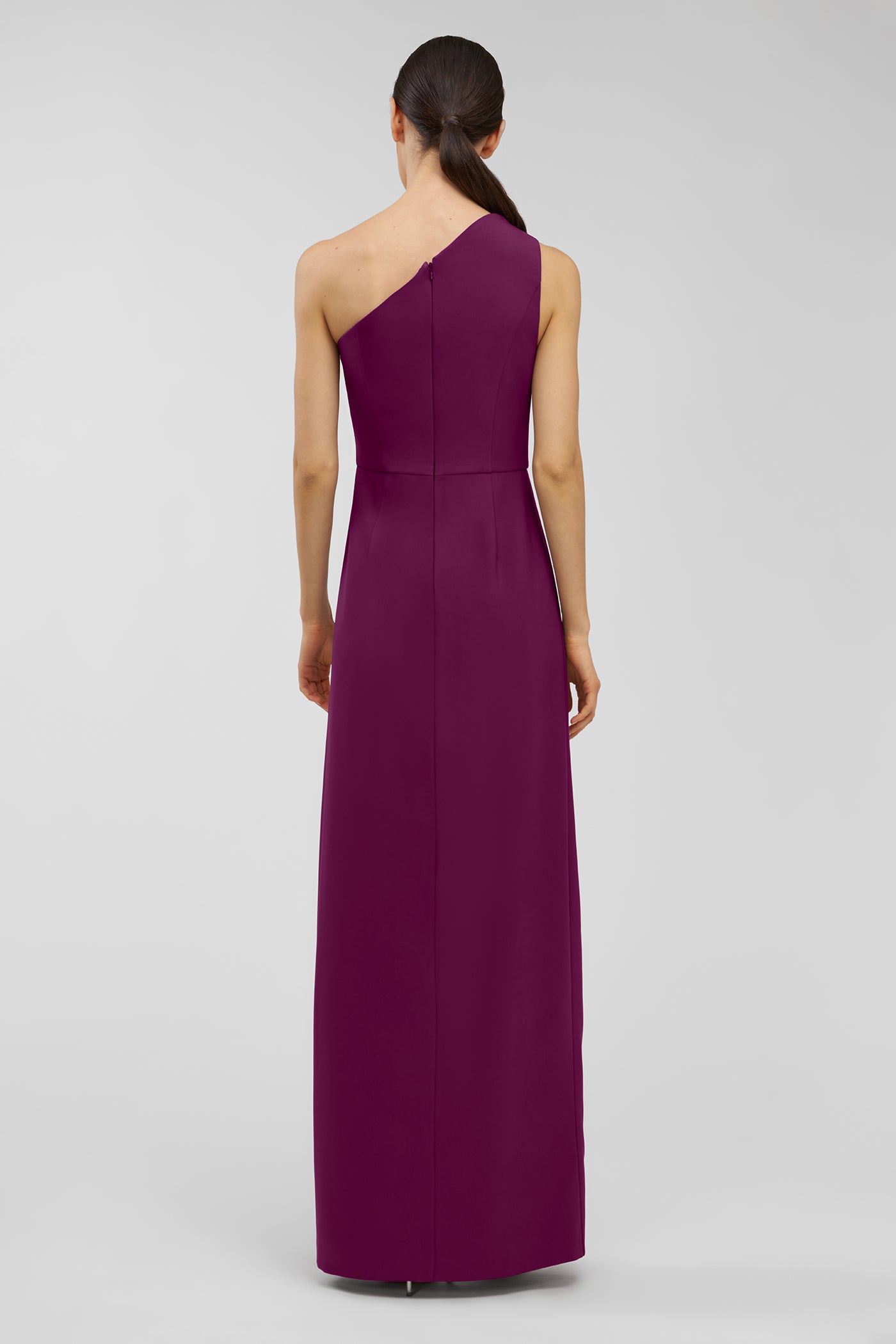 Woman wearing a one-shoulder purple walk thru jumpsuit on a gray background